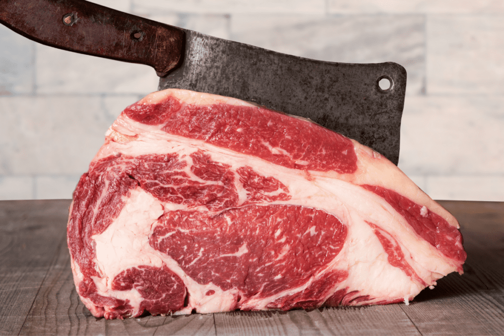 raw prime rib being steak being carved with a cleaver