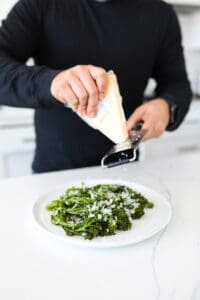 Parmesan cheese being grated on plated broccolini.