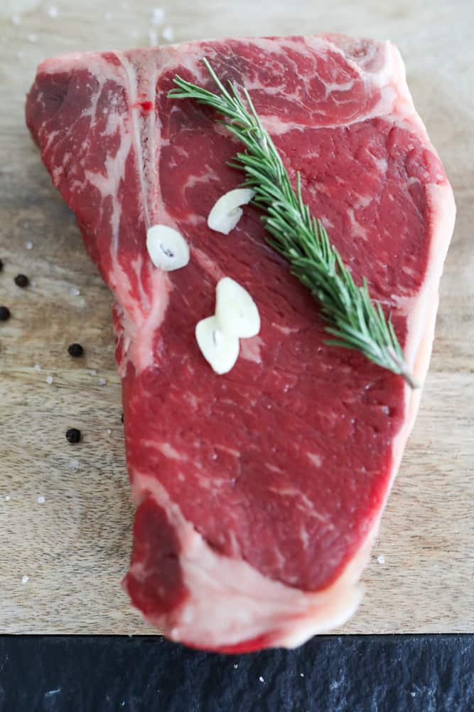 Raw T-bone steak with garlic and rosemary on it.