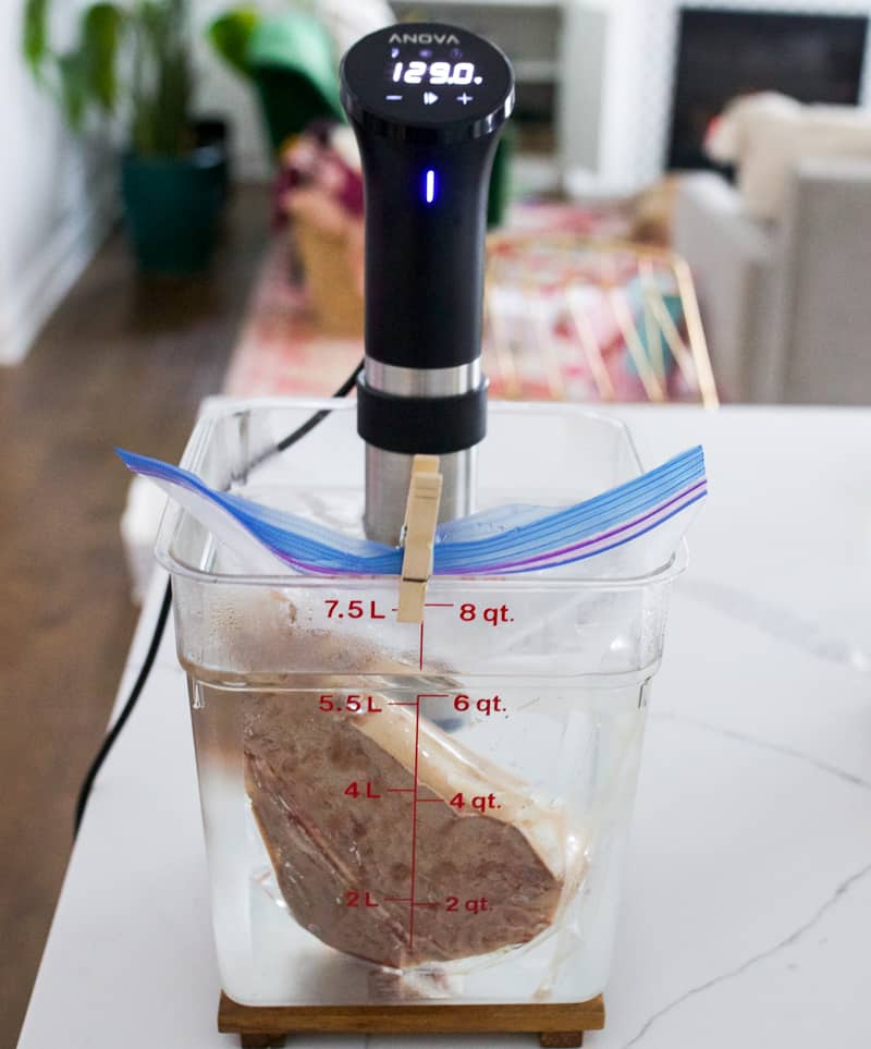 Anova Precision Cooker in a sous vide container full of water with a porterhouse steak in it.