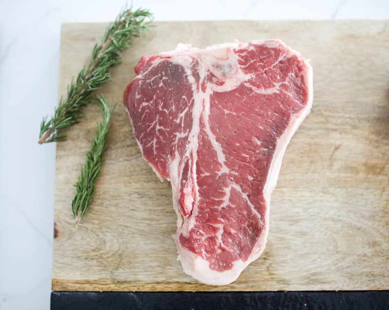 Porterhouse raw on wooden cutting board with two sprigs of rosemary.