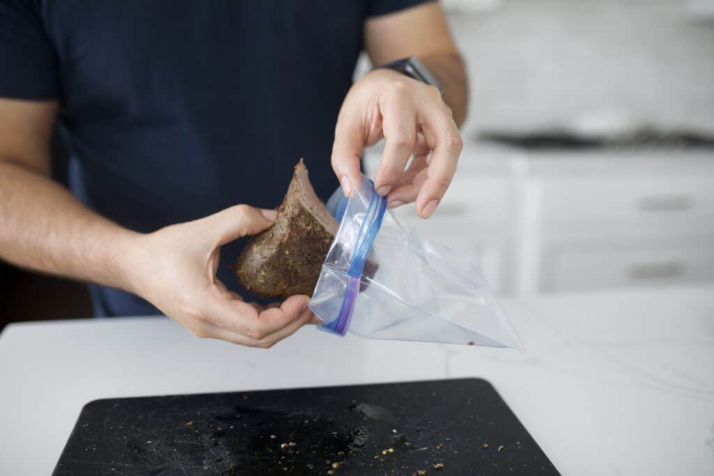 Chunk of steak being placed in a Ziploc bag.