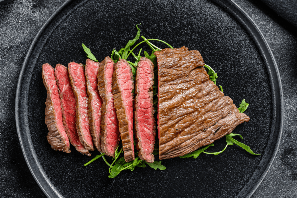 london broil cooked perfectly on a black plate; half sliced to show perfectly cooked edge-to-edge interior