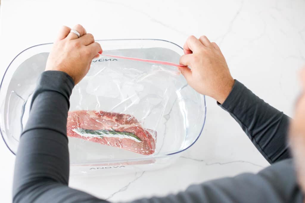 Steak in a Ziploc bag submerged in sous vide container full of water. Over the shoulder shot as bag being closed.