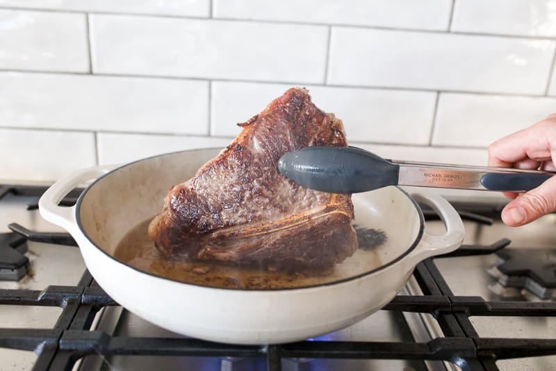 Steak being seared in cast iron pan.