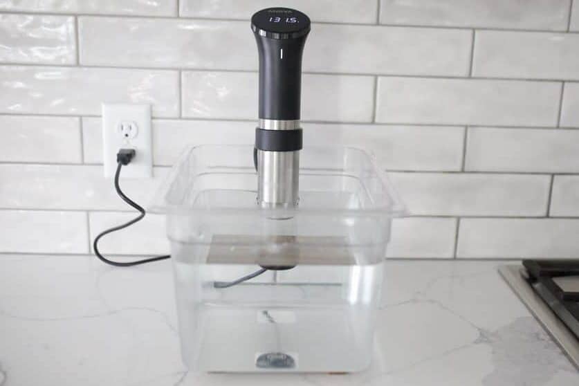 Anova Precision Cooker in a sous vide container full of water.