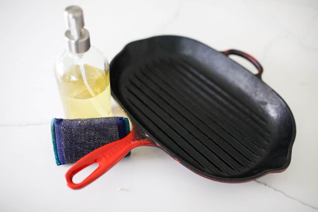Cast iron pan with soap bottle and scouring pad next to it.