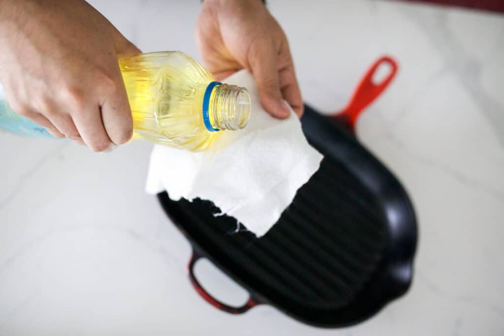 Pouring oil on a microfiber cloth with cast iron skillet in the background.