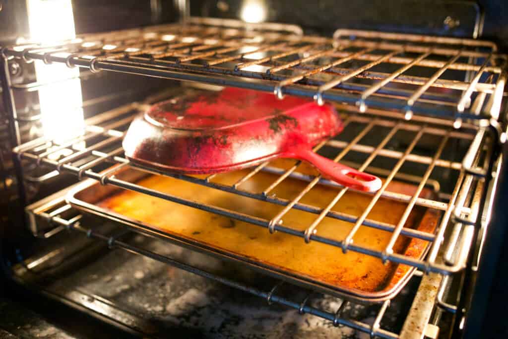 Cast iron in oven upside down with a baking sheet on a lower rack directly beneath it.