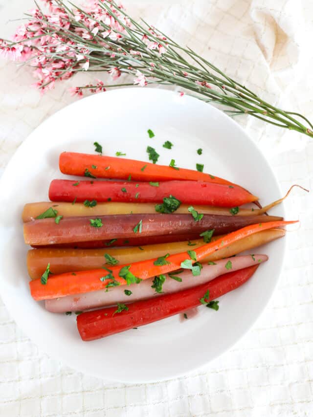 Multi-colored carrots on a white plate. Flowers on the side.