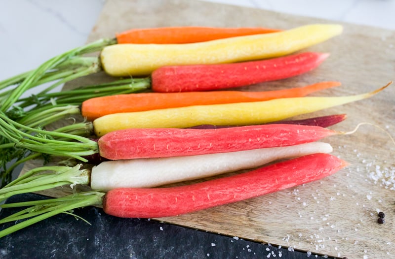 Untrimmed multi-colored carrots on cutting board.
