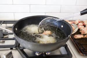 Chicken wings being fried in a wok with a spider strainer moving a wing.