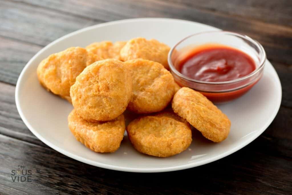 Lightly golden chicken nuggets on a plate with a condiment bowl of ketchup.