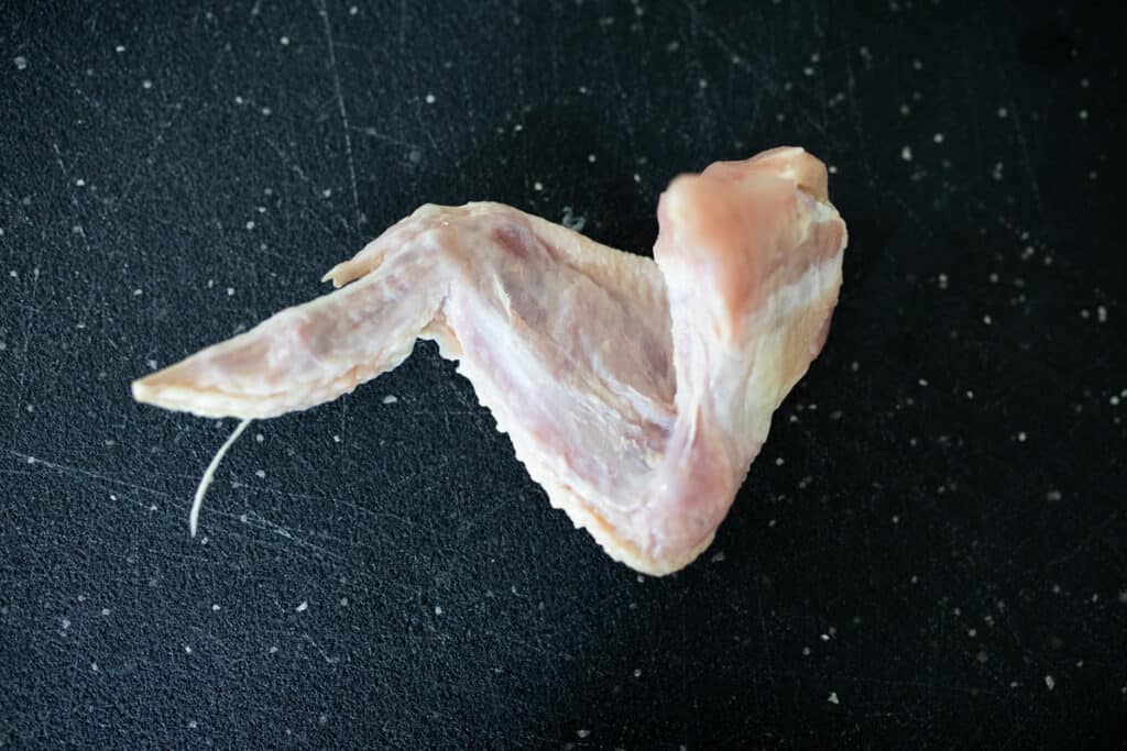 Whole raw chicken wing stretched out so you can see the three distinct parts.