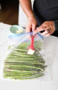 Asparagus in a Ziploc bag with butter being added via red spatula.