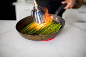 Asparagus in a pan being charred with a Searzall.