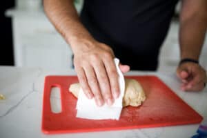 Chicken on a cutting board being dried with a paper towel.