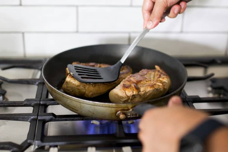 Chicken breast being seared in a pan while pressed with a spatula.