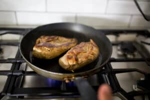 Chicken breast being seared in a pan.