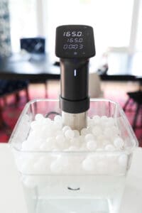 Anova Pro in a sous vide container full of water and floating sous vide balls.