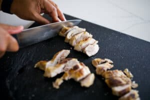 Chicken thighs being sliced on a cutting board.
