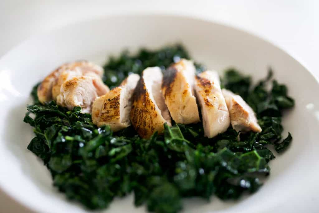 Chicken thigh sliced on a bed of wilted kale in a bowl.