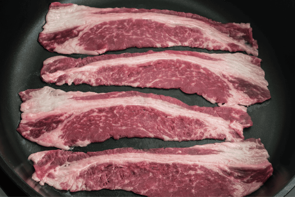Beef bacon strips in a frying pan.