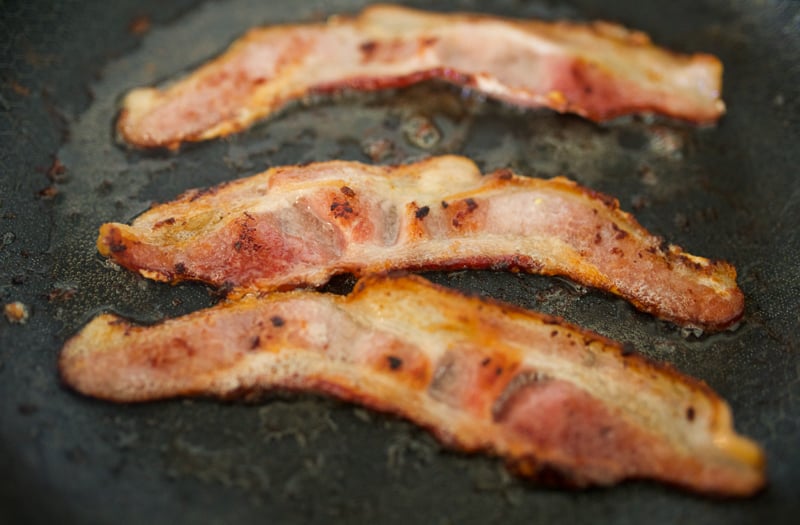 Bacon being cooked in a pan on the stovetop.