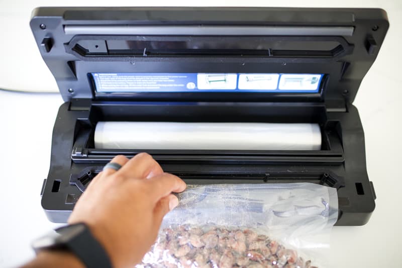 One end of bag full of almonds being placed in vacuum sealer channel.